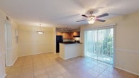 This single-floor residence offers a practical and comfortable layout with an open-concept design that seamlessly connects the living, dining, and kitchen areas. The main living space is finished with large neutral-toned ceramic tile flooring and features a ceiling fan with light fixture, a sliding glass door with vertical blinds that opens to an outdoor view of lush greenery, and a decorative pendant light over the dining area. A chair rail detail runs along the walls, adding a classic architectural touch throughout the common areas.

The kitchen is a standout feature, equipped with warm honey-toned wood cabinetry, dark granite countertops, and a full suite of black appliances including a refrigerator, electric range, and dishwasher. A breakfast bar peninsula provides additional counter space and casual seating, while track lighting overhead and a window with shutters enhance both functionality and natural light.

The bedroom is carpeted for comfort, features its own ceiling fan, and is filled with natural light from a window with blinds. The bathroom is clean and functional, offering a tiled shower and tub combination, a wood-vanity with a white countertop, and tile flooring. Throughout the space, light neutral wall colors and textured ceilings contribute to a bright, cohesive ambiance.