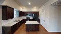 This two-story residence offers a thoughtfully designed layout with warm hardwood-style flooring flowing throughout both levels, neutral wall tones, and ceiling fans in every room for year-round comfort. The main level welcomes you through a front entry door with transom window into a spacious living area filled with natural light from large windows overlooking the surroundings. A staircase with dark wood railing connects the floors.

The kitchen is a standout feature, boasting rich dark espresso cabinetry with brushed nickel hardware, light-toned countertops, a classic white subway tile backsplash, a double stainless steel sink, and a full suite of black appliances including a range, microwave, dishwasher, and refrigerator. A central island provides additional prep and serving space.

The bedrooms are generously sized, each with large windows that invite natural light and ceiling fans overhead. The multiple bedrooms offer flexibility for various living arrangements.

Two full bathrooms serve the home. One features a combination tub and shower with a single vanity and pendant lighting, while the second offers a walk-in shower stall, a matching vanity with dark cabinetry, and a well-lit mirror. Both bathrooms include grab bars and hardwood-style flooring for a cohesive finish throughout the home.