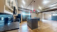 Located at 330 E Ninth St in Saint Paul, MN, this loft-style residence showcases a compelling blend of industrial and modern design elements. The open-concept layout is anchored by warm hardwood flooring that flows throughout the main living area, complemented by exposed brick walls and polished corrugated metal ceilings with visible ductwork that reinforce the space's industrial character. Natural light filters in through transom-style windows, adding brightness to the expansive main area.

The kitchen is thoughtfully appointed with white shaker cabinetry, dark granite countertops, a textured tile backsplash, and a full suite of stainless steel appliances including a side-by-side refrigerator, range, microwave, and dishwasher. A dark-finished island with seating provides additional prep space and a casual dining option, while striking red pendant lights add a bold design accent overhead.

The bathroom features a clean, classic aesthetic with white subway tile, a full soaking tub with shower combination, mosaic tile accents in black and white, and coordinating floor tile. In-unit laundry is conveniently housed in a dedicated space with a stacked front-loading washer and dryer. This loft offers a distinctive urban living experience with thoughtful modern finishes throughout.