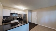 This thoughtfully renovated studio unit presents a seamless open-concept layout that maximizes every inch of available space. The kitchen serves as the centerpiece of the home, showcasing stainless steel appliances including a refrigerator and electric range, rich dark granite countertops, and a striking dark subway tile backsplash that adds depth and character. White shaker-style upper cabinets provide ample storage and contrast beautifully against the darker tones of the kitchen finishes. A peninsula counter extends the workspace and offers a natural divider between the kitchen and the living area, creating a sense of defined zones within the open floor plan. The living area features warm, neutral-toned carpet that transitions seamlessly from the hard flooring near the entry, adding comfort underfoot. A textured ceiling with recessed track lighting illuminates the kitchen area effectively. The entryway is clean and practical, with a solid entry door and a closet providing convenient storage. The overall aesthetic is modern and cohesive, with a neutral color palette that allows for easy personalization. This Phase II renovation reflects quality updates throughout, making it a move-in ready space with contemporary style and everyday functionality.