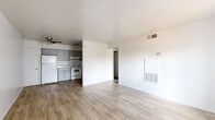 Located at 2550 West Hazelwood Street in Phoenix, AZ, this single-floor, two-bedroom, one-bathroom unit offers a practical and well-organized layout. Light-toned wood-look flooring runs throughout the home, creating a cohesive and clean aesthetic from room to room. The open living area is bright and airy, featuring white walls, a ceiling fan, and a built-in wall heater unit, with natural light streaming in through a window dressed with vertical blinds. The kitchen is efficiently designed in an L-shaped configuration, outfitted with gray cabinetry extending to the ceiling for ample storage, white appliances including a refrigerator and electric range, a single-basin sink, and a dedicated overhead ventilation hood. Both bedrooms are comfortably sized with light flooring, white walls, and windows with vertical blinds that allow for natural light. The primary bedroom includes a closet, while the second bedroom also features a built-in closet with a rod for hanging storage. A hallway connects the main living spaces to the bedrooms and bathroom. The full bathroom includes a vanity with a speckled countertop, a toilet, and a tub-shower combination with clean white surround panels and a chrome curtain rod.