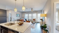 Located at 1500 Laurel Crossing Pkwy NE in Buford, Georgia, this single-floor residence offers a thoughtfully designed open-concept layout that seamlessly connects the kitchen, dining, and living areas. The kitchen is outfitted with dark shaker-style cabinetry, stainless steel appliances, light granite countertops, a subway tile backsplash, and wood-look flooring, providing both functionality and style. Pendant lighting over the kitchen island adds a warm, modern touch. The open living area is bright and inviting, featuring wood-look hardwood flooring, a ceiling fan, and large windows with blinds and curtain panels that allow abundant natural light to fill the space. A glass-paned door leads to an outdoor access point. The bedroom features plush carpet, generous natural light through large windows, and a ceiling fan for year-round comfort. A dedicated walk-in closet with built-in rod and shelving provides ample storage. The bathroom includes dark vanity cabinetry, a tiled soaking tub-shower combination, and wood-look flooring. A separate in-unit laundry closet houses a full-size washer and dryer with overhead shelving. Throughout, the residence maintains a clean, neutral color palette that creates a cohesive and modern living environment.