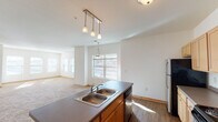 This single-floor residence is designed with a practical, open-concept layout that connects the kitchen, dining, and living areas into one cohesive space. The kitchen is well-equipped with light maple cabinetry offering generous storage, dark countertops, stainless steel appliances including a refrigerator and over-the-range microwave, and a black electric range. A peninsula with a double-basin sink and pendant lighting above serves as both a functional workspace and a natural divider between the kitchen and the adjoining dining and living areas.

The expansive living area is finished with plush neutral carpeting and is bathed in natural light from multiple windows. A vaulted ceiling accent adds architectural interest, and a glass-paned door provides direct access to a private outdoor deck. The bedrooms are carpeted and feature ample closet space, including a notably generous walk-in closet outfitted with wire shelving and hanging rods. Two full bathrooms each include a tub-shower combination, wood-look flooring, warm-toned vanity cabinetry, and dark countertops. Throughout the residence, warm wood-tone trim and neutral walls contribute to a clean, understated aesthetic.