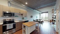 Located in Seattle's South Lake Union neighborhood, this single-floor unit at 624 Yale Avenue North blends industrial design with contemporary comfort. The open-concept layout is defined by striking exposed concrete ceilings with visible ductwork, rich hardwood flooring, and expansive floor-to-ceiling windows that flood the space with natural light and frame views of the surrounding cityscape.

The kitchen is thoughtfully equipped with stainless steel appliances — including a refrigerator, range, microwave, and dishwasher — complemented by light wood cabinetry, white countertops, and a butcher block island that provides additional prep and storage space. The kitchen flows seamlessly into the dining and living areas, creating a cohesive and functional gathering space.

The living room offers generous proportions with an open, airy feel, anchored by a sectional sofa and accented by the raw architectural detail of the concrete ceiling above. The bedroom features soft carpeting, a large closet, and windows that continue the theme of bringing in abundant natural light and outdoor views. A dedicated workspace nook adds practical versatility to the layout.

The bathroom is finished with wood-toned cabinetry, a combination tub and shower, a single vanity with a large mirror, and wood-look flooring, completing this well-appointed urban residence.