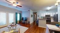 This single-floor residence offers a thoughtfully designed layout that balances open communal living with private bedroom spaces. The living room serves as the heart of the home, featuring rich hardwood flooring, crown molding, and a ceiling fan. Natural light filters in through sliding glass doors and teal-curtained windows, while the open floor plan creates a seamless connection to the kitchen and dining area.

The kitchen is well-equipped with white cabinetry, stainless steel appliances including a range, microwave, dishwasher, and refrigerator, all set above continued hardwood flooring. A breakfast bar with seating provides a convenient casual dining option.

The residence includes two bedrooms, each with ceiling fans, hardwood floors, and windows with blinds. The first bedroom offers a cozy, well-lit atmosphere with a wall shelf and ample space. The second bedroom features track lighting and a dedicated workspace area.

Two bathrooms serve the home, each featuring a single-sink vanity with white cabinetry, a mirror, and hardwood flooring. The overall color palette of soft blue-gray walls paired with warm wood tones creates a calm, cohesive ambiance throughout the entire residence.