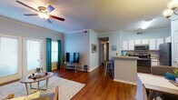 This single-floor residence offers a thoughtfully designed layout that balances open communal living with private bedroom spaces. The living room serves as the heart of the home, featuring rich hardwood flooring, crown molding, and a ceiling fan. Natural light filters in through sliding glass doors and teal-curtained windows, while the open floor plan creates a seamless connection to the kitchen and dining area.

The kitchen is well-equipped with white cabinetry, stainless steel appliances including a range, microwave, dishwasher, and refrigerator, all set above continued hardwood flooring. A breakfast bar with seating provides a convenient casual dining option.

The residence includes two bedrooms, each with ceiling fans, hardwood floors, and windows with blinds. The first bedroom offers a cozy, well-lit atmosphere with a wall shelf and ample space. The second bedroom features track lighting and a dedicated workspace area.

Two bathrooms serve the home, each featuring a single-sink vanity with white cabinetry, a mirror, and hardwood flooring. The overall color palette of soft blue-gray walls paired with warm wood tones creates a calm, cohesive ambiance throughout the entire residence.
