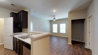 This 2-bedroom, 1-bathroom residence is thoughtfully designed on a single floor, offering an efficient and comfortable open-concept layout. The kitchen features dark espresso cabinetry that provides a striking contrast against the light countertops, and includes a built-in sink and dishwasher. A peninsula counter extends outward, creating a natural divider between the kitchen and the adjoining living area while offering additional workspace and casual seating potential. The living area is bright and welcoming, with multiple windows that allow natural light to fill the space. A ceiling fan overhead adds both functionality and a finishing touch to the room. Rich, dark hardwood-style flooring runs throughout the main living areas, adding warmth and a sense of continuity to the space. Neutral wall tones complement the overall design, creating a clean and versatile backdrop. The open flow between the kitchen and living room makes the home feel spacious and well-connected, ideal for everyday living and entertaining. A hallway leads to the private bedroom and bathroom areas, maintaining a clear separation between living and sleeping spaces.