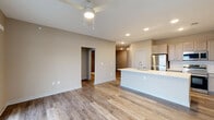 Located at 5813 Lilliana Ln in Whitestown, Indiana, this 2-bedroom, 3-bathroom single-floor residence offers a well-designed layout with modern finishes throughout. The open-concept kitchen and living area serves as the heart of the home, anchored by a central island with a white quartz countertop and undermount sink, stainless steel appliances, tile backsplash, and taupe cabinetry with recessed lighting above. Light-toned luxury vinyl plank flooring runs throughout the main living areas, complemented by neutral warm-beige walls. The living area is bright and airy, featuring a ceiling fan, large windows with blinds, and sliding glass doors with transom windows above that open to a private balcony with scenic outdoor views. Both bedrooms are carpeted and include ceiling fans; the primary bedroom offers a generous footprint and connects to a bathroom with a vanity featuring blue-gray cabinetry, white countertop, built-in shelving, and a tiled walk-in shower. The additional bathrooms are equally well-appointed with matching finishes. The unit also includes multiple closets providing ample storage, a dedicated laundry area, and connecting hallways that give the layout a functional, organized flow.