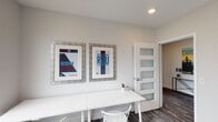 Located at 5710 Hillsborough St in Raleigh, NC, this single-floor space is designed as a functional and inviting collaborative environment. The layout consists of two distinct areas: a focused study room and a larger meeting or gathering room, connected by interior doorways fitted with sleek, frosted-glass panel doors that allow light to pass between spaces while maintaining privacy.

The study area features a long white work surface paired with white Windsor-style chairs, comfortably accommodating multiple users. A large window overlooks the surrounding neighborhood, providing ample natural light. The walls are adorned with locally inspired RDU-themed framed artwork, adding a sense of Raleigh identity to the space.

The adjacent meeting room centers around a natural wood table surrounded by a mix of white and teal seating. A wall-mounted flat-screen television makes this room well-suited for presentations or group collaboration. Multiple large windows offer views of the neighboring community and fill the room with daylight.

Throughout both rooms, multi-toned patterned carpet in gray and charcoal tones grounds the clean, neutral palette of white walls and modern trim. Recessed lighting supplements natural light, ensuring a bright and productive atmosphere. The overall design is clean, contemporary, and thoughtfully curated for community use.