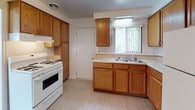 This 3-floor residential property offers a practical and well-structured layout across its levels. The kitchen is equipped with warm oak cabinetry extending to the ceiling for ample storage, a white gas range, a double-basin sink positioned beneath a window with vertical blinds, and light vinyl flooring. A door provides direct exterior access, adding convenience to the space.

The main living areas feature wall-to-wall carpet in a neutral beige tone, complemented by warm tan walls and clean white crown molding and baseboards throughout. Large windows dressed with vertical blinds allow generous natural light to fill these open rooms. One of the living areas connects directly to the kitchen, creating a flowing layout ideal for everyday use.

The bedrooms continue the same carpeted, light-filled aesthetic, each with windows and ceiling-mounted light fixtures. At least one bedroom includes a built-in closet with shelving and a hanging rod, providing organized storage.

The bathroom features a full bathtub and shower combination with floor-to-ceiling neutral gray square tile work, a grab bar, and a corner shelf for practical functionality.

The basement level is unfinished, with an exposed ceiling, concrete flooring, small hopper windows, and a utility sink — offering significant potential for storage or future development.