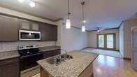 This single-floor residence offers a thoughtfully designed open-concept layout that seamlessly connects the kitchen and living areas. The kitchen is a standout feature, showcasing dark espresso-toned cabinetry with shaker-style doors, granite countertops, a classic white subway tile backsplash, and a full suite of stainless steel appliances including a refrigerator, electric range, and built-in microwave. A central island with an undermount sink and pendant lighting above adds both functionality and visual appeal. Light hardwood-style flooring flows throughout the main living areas, complemented by crown molding that lends a refined touch.

The living area is generously proportioned, featuring a ceiling fan and French doors that invite natural light and provide outdoor access. Each bedroom is carpeted for comfort, equipped with a ceiling fan, and receives natural light through blinded windows with views of the surrounding neighborhood.

The bathrooms are finished with granite-topped vanities, dark cabinetry, and warm tile flooring. One bathroom includes a walk-in glass shower. A dedicated in-unit laundry room houses a full-size top-loading washer and dryer with overhead shelving for added storage. The cohesive design and quality finishes make this a comfortable and functional living space.