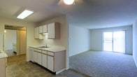 This single-floor space presents an open-concept layout that seamlessly connects the kitchen and living area. The kitchen is outfitted with white cabinetry offering ample upper and lower storage, a double-basin sink set into a light-colored countertop, and dark tile flooring that adds contrast and durability underfoot. A range hood is mounted beneath the upper cabinets, and the space accommodates standard appliances. The transition from the kitchen's tile flooring to the living area's neutral wall-to-wall carpet creates a clear, natural division between the two zones. The living area is generously proportioned, featuring light-toned walls that contribute to a bright and airy atmosphere. A sliding glass door or large window at the far end of the living space invites natural light deep into the interior, enhancing the overall sense of openness. The ceilings are smooth and of standard height throughout, and a centrally mounted ceiling light fixture provides overhead illumination. The overall design is clean and understated, emphasizing practicality and ease of use within a cohesive, connected floor plan.
