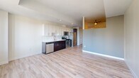 Located at 100 Steele St in Denver's vibrant Cherry Creek neighborhood, this single-floor residence offers a clean, contemporary design throughout. The open-concept layout connects the kitchen and living area seamlessly, creating a bright and functional living space. Light wood-style flooring runs throughout, complementing the neutral gray and white color palette that lends the unit a modern, airy feel.

The kitchen is well-appointed with white shaker-style upper cabinets, dark espresso lower cabinets, and quartz countertops. A classic white subway tile backsplash adds texture, while a full suite of stainless steel appliances — including a gas range, refrigerator, dishwasher, and microwave — ensures a fully equipped cooking space. A deep undermount sink with a sleek faucet completes the setup.

The living area is generously proportioned, featuring a ceiling fan and recessed lighting. A hallway leads to a private bedroom that benefits from a large window framing expansive city views of the Denver skyline. Natural light fills the space, highlighting the clean lines and well-maintained finishes. The entry corridor provides a defined transition from the front door into the open living areas, adding to the overall sense of flow and practicality throughout this thoughtfully designed urban residence.