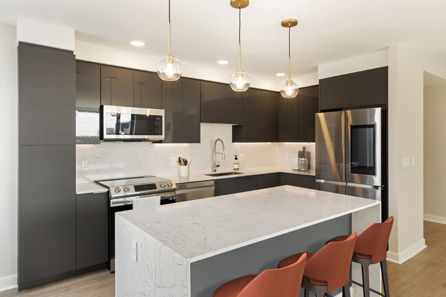 Renovated Package I kitchen with grey cabinetry, white marbled quartz countertops and backsplash, stainless steel appliances, and hard surface flooring - Avalon Exeter