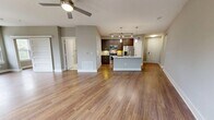 This 980-square-foot, two-bedroom, two-bathroom apartment at 2401 Aldrich Street in Austin, TX offers a well-designed single-floor layout with modern finishes throughout. The open-concept kitchen and living area serves as the heart of the unit, featuring rich hardwood flooring, a central island with a marble-style countertop and undermount sink, dark espresso cabinetry, stainless steel appliances including a refrigerator, range, and built-in microwave, and pendant and track lighting overhead. The living room is bathed in natural light from a bank of four large windows and includes a ceiling fan. The primary bedroom, at 170 square feet, offers plush carpeting, a ceiling fan, and access to a walk-in closet with built-in shelving and hanging rods. The second bedroom features hardwood floors and two windows with views of surrounding greenery. Both bathrooms are finished with large-format white tile flooring and dark wood vanities with stone countertops. The hallway connecting the rooms provides a clean, functional transition between spaces. Neutral gray walls and white trim are consistent throughout, creating a cohesive, contemporary aesthetic well-suited to urban Austin living.