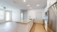 This single-story, 2-bedroom, 2-bathroom residence offers a clean, modern aesthetic with a practical layout designed for comfortable everyday living. The open-concept kitchen serves as the heart of the home, featuring granite countertops, a large center island with an undermount sink, white shaker-style cabinetry, a subway tile backsplash, and a full suite of stainless steel appliances including a refrigerator, range, and microwave. Light wood-style flooring runs throughout the main living areas, complementing the bright, neutral color palette. The living room is bathed in natural light through windows and a glass door that connects the space to the outdoors, with a ceiling fan adding practical comfort. Both bedrooms are carpeted and generously sized, each featuring large windows with blinds and ceiling fans. The primary bedroom includes a dedicated closet with wire shelving for organized storage. The bathrooms are finished with granite-topped vanities, wood-style flooring, and a tiled tub-shower combination with classic white subway tile. A dedicated laundry room houses a full-size washer and dryer. Recessed lighting throughout enhances the bright, airy feel of this well-designed residence.