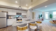Located at 6650 Liberty Grand Blvd. in Powell, Ohio, this two-floor home offers a thoughtfully designed layout with modern finishes throughout. The open-concept kitchen serves as the heart of the main level, showcasing striking granite countertops with bold veining, crisp white cabinetry, stainless steel appliances, and a large center island with an integrated sink and seating — illuminated by stylish pendant lights overhead. Warm hardwood-style flooring anchors the kitchen and flows into the adjoining dining and entertaining areas. The spacious living room features plush carpeting, crown molding, recessed lighting, and large windows that invite abundant natural light, creating an inviting and comfortable atmosphere. A secondary sitting or dining nook adds functional flexibility to the main level. Upstairs, the bedroom suite is highlighted by vaulted ceilings and generous windows that brighten the room naturally. Soft carpeting and a serene color palette give the space a restful quality. A well-appointed bathroom with blue-gray cabinetry and a dual vanity is conveniently accessible from the upper hallway. Additional rooms and utility spaces round out the floor plan, providing practical storage and laundry accommodations. Overall, this home blends contemporary style with comfortable livability.