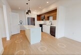 This 640-square-foot, one-bedroom, one-bathroom apartment at 3585 Aero Ct in San Diego, CA 92123 offers a thoughtfully designed modern living experience. The open-concept kitchen and living area serves as the heart of the unit, featuring light hardwood-style flooring throughout, recessed lighting, and sleek pendant lights above a white kitchen island with a quartz countertop. The kitchen is appointed with two-tone cabinetry — crisp white lower cabinets paired with warm wood upper cabinets — complemented by a white subway tile backsplash, stainless steel gas range, over-the-range microwave, dishwasher, and a full-size refrigerator. The 150-square-foot primary bedroom is bright and airy, equipped with a ceiling fan and large windows that invite abundant natural light and urban views of the surrounding San Diego skyline and neighborhood. The bathroom features a clean, contemporary design with a wood-accented vanity, white countertop, full soaking tub with tiled surround, and a curved shower rod. Additional spaces include a closet and hallway, maximizing the unit's functional layout. White walls and consistent light flooring create a cohesive, modern aesthetic throughout this well-appointed San Diego apartment.