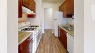 Located at 18215 Lost Knife Cir in Montgomery Village, MD, this two-bedroom, one-bathroom single-floor home offers a practical and well-organized layout. The galley-style kitchen is equipped with rich dark wood cabinetry, granite-style countertops, a gas range, white appliances including a dishwasher and refrigerator, and durable wood-look flooring. A chandelier-lit dining or living area is visible just beyond the kitchen, adding warmth to the space. The living area features plush carpeting, a large sliding glass door with vertical blinds that invites natural light, and access to additional closet storage. Both bedrooms are carpeted and finished in neutral tones with ample natural light from multiple windows. The spacious primary bedroom includes a walk-in closet and an additional closet, providing generous storage. The second bedroom also features a standard closet. The full bathroom includes a tiled shower-tub combination with clean white finishes. Hallways connect the rooms efficiently, and the overall layout makes thoughtful use of the available square footage. The home's neutral color palette and consistent finishes throughout create a clean, move-in ready aesthetic suitable for a variety of living arrangements.
