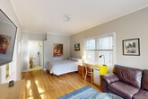 Located at 903 Seventh St in Santa Monica, CA, this well-organized one-bedroom, one-bathroom unit offers an efficient and functional single-floor layout. The spacious main room features warm hardwood flooring, crown molding, and a ceiling fan, creating a comfortable and inviting atmosphere. Multiple windows allow abundant natural light to fill the space, with views of the surrounding neighborhood. The room comfortably accommodates a full-sized bed, a dedicated workspace with a desk and chair, and a seating area with a leather sofa and coffee table — making it a versatile living environment. Colorful wall art adds a cheerful, personal touch throughout. The separate kitchen is equipped with full-sized cabinetry featuring wood trim, a refrigerator, microwave, and tiled countertops, along with a small dining area. The bathroom is clean and bright, finished with classic white hexagonal floor tile, a pedestal-style sink with wood vanity, wall-mounted storage cabinet, and a mirrored medicine cabinet. A small window provides natural ventilation. Situated in a prime Santa Monica location, this unit offers convenient access to the beach, dining, shopping, and public transportation.