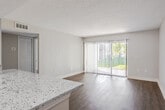 Located in Saint Petersburg, Florida, this single-story residence presents a thoughtfully designed open-concept floor plan finished with consistent wood-look flooring and neutral tones throughout. The living area is spacious and well-lit, anchored by a full-width sliding glass door fitted with vertical blinds that open to an outdoor view of lush greenery, allowing natural light to fill the space generously. Textured ceilings add a classic architectural detail visible across all rooms.

The kitchen is a standout feature, showcasing granite countertops with a sweeping breakfast bar peninsula that connects seamlessly to the living area. White cabinetry provides ample storage, while stainless steel appliances—including a range, microwave, and refrigerator—lend a modern, polished finish. A skylight positioned above the kitchen brightens the workspace naturally.

A dedicated dining area adjacent to the kitchen offers additional flexibility, also benefiting from a window with outdoor views. The bedrooms are well-proportioned, each featuring wood-look flooring, vertical blinds on windows, and closet storage. The overall ambiance is clean, bright, and move-in ready, reflecting a cohesive and functional interior design.