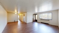 This single-floor residence is laid out across a practical, well-organized floor plan that accommodates a variety of living arrangements. Hardwood-style flooring runs throughout the unit, providing a warm and cohesive aesthetic across every room.

The open living area is generously sized, filled with natural light streaming through large windows that offer outdoor views. A glazed entry door adds an additional source of light and character to the main living space, which also features a ceiling fan with integrated lighting and a radiator heating unit.

The kitchen is well-appointed with warm oak cabinetry extending to the ceiling, offering substantial storage. White appliances include a four-burner electric range, dishwasher, and refrigerator, complemented by a window overlooking greenery outside. Counter space lines both sides of the galley-style layout.

The bedrooms are spacious and bright, each featuring hardwood-style flooring, ceiling fans, and windows with exterior views. One bedroom includes a roomy closet with a hanging rod. Additional rooms offer flexible use as a bedroom or living space.

The bathroom retains a classic character with white and mint-green tiled walls surrounding a full soaking tub with a handheld showerhead and a natural light window.
