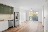 Located on Harbor Blvd in Costa Mesa, CA, this single-floor unit showcases a clean, modern design throughout. Light hardwood flooring runs continuously across the open layout, contributing to a cohesive and airy aesthetic.

The kitchen is a standout feature, equipped with glossy teal upper cabinetry contrasted by crisp white lower cabinets and stone-look countertops. A classic subway tile backsplash complements the full suite of stainless steel appliances, including a gas range, built-in microwave, dishwasher, and French door refrigerator. Recessed lighting enhances the workspace. An adjacent entry area provides a practical transition space with additional cabinetry.

Multiple bedrooms offer generous natural light through large sliding and fixed windows framing outdoor greenery and neighborhood views. One bedroom features sliding glass doors opening directly to a private balcony, accompanied by a ceiling fan. Additional bedrooms benefit from multiple windows and bright, neutral walls.

The bathrooms are finished with large-format marble-look stone tile, frameless glass shower enclosures over soaking tubs, backlit vanity mirrors, and warm wood-toned cabinetry, delivering a polished, spa-inspired atmosphere throughout.