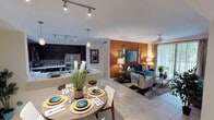 This well-appointed single-floor residence showcases a thoughtfully designed open-concept layout that seamlessly connects the living, dining, and kitchen areas. The kitchen is outfitted with dark espresso cabinetry, stainless steel appliances including a side-by-side refrigerator and range, a mosaic tile backsplash, white countertops, and track lighting — all finished with light tile flooring that carries through the main living areas. Adjacent to the kitchen, the dining area features a bold yellow accent wall and a circular dining table with bar seating along the kitchen counter. The living room makes a strong visual statement with a warm terracotta accent wall, crown molding, a ceiling fan, and a sliding glass door that opens to an outdoor area with lush greenery views. The primary bedroom features rich carpet flooring, a deep navy accent wall, natural light from multiple windows, and a ceiling fan. A second bedroom continues the warm color palette with a rust-toned accent wall and ample natural light. Two full bathrooms serve the unit, each with a soaking tub and shower combination, tile surrounds, dark vanity cabinetry, and white countertops. The overall design blends bold color accents with modern fixtures to create a dynamic and cohesive living environment.