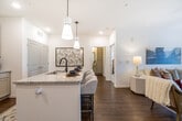 This thoughtfully designed single-floor residence offers a bright, open-concept layout that seamlessly connects the kitchen, dining, and living areas. The kitchen is a standout feature, equipped with white shaker-style cabinetry, stainless steel appliances, a subway tile backsplash, and granite countertops that extend to a generously sized island with seating — ideal for casual dining. Elegant pendant lighting illuminates the island, while recessed lighting and wood-look flooring carry throughout the main living areas. The living room is a comfortable and inviting space, featuring a ceiling fan, draping curtains, and glass French doors that invite natural light and provide outdoor access. The bedrooms are carpeted and well-proportioned, each offering a calm, neutral palette. One bedroom connects to a walk-in closet outfitted with multi-tier wire shelving and hanging rods, providing ample storage. The bathroom features granite countertops, gray cabinetry, a large vanity mirror, and a full tub-shower combination, with wood-look flooring tying the space together. Throughout the residence, a consistent use of white walls, granite surfaces, and warm wood-tone flooring creates a cohesive and modern aesthetic.