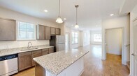 Located at 2024 Barr Road in Concord, NC, this two-story home offers a well-designed layout across two floors. The main level provides generous living space, anchored by an open-concept kitchen and living room that flows seamlessly together. The kitchen is a standout feature, showcasing granite countertops, rich dark cabinetry, a central island with pendant lighting, and a full suite of stainless steel appliances including a refrigerator, range, dishwasher, and microwave. Light hardwood flooring runs throughout, complemented by recessed lighting and an abundance of natural light from multiple windows. The living area benefits from vaulted ceilings, creating an airy, open ambiance. An attached garage and a dedicated laundry room with washer and dryer add everyday convenience. Upstairs, the primary bedroom is a comfortable retreat featuring vaulted ceilings, multiple windows with outdoor views, a ceiling fan, and direct access to a private en-suite bathroom with a glass-enclosed shower, granite vanity, and a spacious walk-in closet. Two additional bedrooms and two more full bathrooms round out the home. With five closets total and a thoughtful floor plan, this home balances practicality with comfortable living in a well-appointed Concord setting.