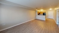 Located at 95 Burnett Ave S, Unit 218 in Renton, WA, this single-floor residence presents a clean, modern aesthetic with consistent light wood-tone luxury vinyl plank flooring and neutral warm-beige walls throughout. The open-concept living and dining area is generously proportioned, offering a seamless flow between living space and the adjacent kitchen. Large windows fitted with horizontal blinds invite abundant natural light, providing views of surrounding greenery.

The kitchen is well-appointed with warm honey-toned wood cabinetry offering ample storage, granite-look countertops, and a breakfast bar peninsula that connects it to the main living area. Black appliances — including a refrigerator, electric range, and over-the-range microwave — provide a clean contrast against the cabinetry, while a double-basin sink completes the practical workspace.

The bedroom features the same plank flooring, a bright window with outdoor views, and a closet with louvered doors, offering a calm and comfortable retreat. An additional room provides flexibility as a bedroom or office, also benefiting from natural light. Clean white trim and baseboards frame each room, contributing to the overall crisp, move-in-ready presentation of this well-maintained Renton residence.