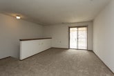 This single-floor unit offers a practical and functional layout spread across several well-defined areas. The living space is generously sized, featuring wall-to-wall carpet in a neutral beige tone, white walls, and a textured ceiling. A ceiling fan with a light fixture provides both comfort and illumination, while a sliding glass door with vertical blinds invites natural light and offers access to the exterior. A half-wall with a wood-capped railing borders the staircase entry, adding a subtle architectural detail to the open space.

The galley-style kitchen is efficiently organized with oak cabinetry lining both sides, laminate countertops, a stainless steel sink, and wood-look vinyl flooring. White appliances—including a coil electric range, refrigerator, and dishwasher—are all in place, and under-cabinet lighting enhances workspace visibility.

The bedroom is a comfortable, carpeted room with a ceiling fan, a window providing natural light, and a closet with mirrored sliding doors. The full bathroom features a tub and shower combination with tiled surround, a toilet, and wood-look flooring, maintaining a clean, functional aesthetic. Throughout the unit, dark wood baseboards provide a consistent finishing detail that ties the spaces together.