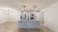 This single-story, 3-bedroom, 3-bathroom home delivers a clean, modern aesthetic with a practical open-concept layout. The heart of the home is a stylish kitchen featuring white shaker-style cabinetry, stainless steel appliances, a granite-topped island with bar seating, and sleek pendant lighting — all flowing seamlessly into the combined dining and living areas. Light wood-look flooring runs throughout the main living spaces, enhancing the bright and airy atmosphere, while a ceiling fan adds comfort to the living room, which opens to a private exterior door with natural light from flanking windows. Each of the three bedrooms is finished with plush neutral carpet and ceiling fans, offering a comfortable retreat. The spacious primary bedroom is complemented by a walk-in closet outfitted with wire shelving for organized storage. The bathrooms echo the home's refined palette with granite vanity countertops and white cabinetry. Two dedicated closet spaces add further storage convenience. The consistent use of neutral tones, clean lines, and quality finishes throughout creates a cohesive and inviting living environment well-suited for everyday comfort.