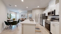 This single-floor residence offers a thoughtfully designed open-concept layout that seamlessly connects the kitchen, dining, and living areas. The kitchen is a standout feature, outfitted with crisp white shaker cabinets, stainless steel appliances including a refrigerator, range, and over-the-range microwave, and a central island with a built-in sink and white quartz countertop — ideal for both meal preparation and casual dining. Light wood-look flooring runs throughout the main living areas, contributing to a clean, contemporary aesthetic.

The living room is bright and welcoming, with large windows that invite natural light and a ceiling fan overhead. The space comfortably accommodates a seating arrangement and opens to the dining area for a cohesive flow.

Two bedrooms provide comfortable private retreats, each with light-toned flooring and windows offering outdoor views. One bedroom features a walk-in closet with wire shelving and dedicated washer/dryer hookups in a separate utility space nearby.

The bathroom is finished with large-format marble-look tile flooring, a white vanity with storage cabinetry, a framed mirror, and modern chrome fixtures — delivering a clean, polished look. Neutral wall tones throughout the residence create a calm, versatile backdrop suited to a variety of design preferences.