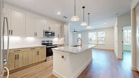 This thoughtfully designed single-floor home offers three bedrooms, two bathrooms, and a comfortable, well-appointed layout. The open-concept kitchen and living area serves as the heart of the home, showcasing a large central island topped with granite countertops, a deep basin sink, and pendant lighting overhead. Cabinetry blends crisp white uppers with warm natural wood lower cabinets, all accented by sleek matte black hardware. Stainless steel appliances, including a range and built-in microwave, complete the kitchen. Light wood-tone flooring flows seamlessly throughout the entire home, lending warmth and visual continuity.

The living room is bright and airy, benefiting from large windows and a glass door that invite abundant natural light and views of the surrounding exterior. A ceiling fan adds comfort to the space. The primary bedroom offers a generous footprint with its own walk-in closet featuring built-in shelving and hanging rods. Additional bedrooms are well-sized with ample natural light and closet storage. The bathrooms are finished with granite-topped vanities, white shaker cabinetry, matte black fixtures, and a tub-shower combination. Clean white walls and recessed lighting throughout contribute to a bright, modern ambiance.