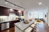 Located at Century Square in College Station, TX, this well-appointed 2-bedroom, 3-bathroom residence offers a thoughtfully designed single-floor layout. The open-concept kitchen and living area serves as the heart of the home, anchored by a granite-topped island with bar seating. Rich dark cabinetry, a white subway tile backsplash, stainless steel appliances — including a refrigerator, range, microwave, and dishwasher — and track lighting complete the kitchen. Gleaming hardwood floors extend throughout the main living area, which features large windows that invite abundant natural light and views of the surrounding greenery. The living room offers a comfortable, airy atmosphere with recessed lighting and clean white walls. The primary bedroom features plush carpet, a ceiling fan, and direct access to a spacious en-suite bathroom outfitted with a dual-sink granite vanity, tile flooring, and an adjacent walk-in closet. The second bedroom is equally well-appointed with soft carpet and a ceiling fan. Two additional bathrooms serve the home, each finished with granite countertops and dark cabinetry. An in-unit washer and dryer provide added convenience, rounding out this polished and functional residence.
