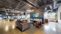 Located at 18807 8th Ave NE in Shoreline, Washington, this expansive single-floor community space delivers an impressive industrial-modern aesthetic across a generously sized open-plan layout. Polished concrete floors reflect light throughout, complementing the exposed ductwork and structural ceiling elements that define the raw, contemporary character of the space.

The layout is organized into distinct yet seamlessly connected zones. A lounge area anchors one section with plush sectional sofas, leather armchairs, and a large wall-mounted display set against a richly textured dark feature wall, illuminated by striking circular pendant lighting. Adjacent to this is a casual seating area with a mix of modular sofas and natural wood accent pieces, fostering a relaxed communal atmosphere.

A dedicated social and entertainment zone includes a full-size billiards table, high-top bar tables with stools, and additional lounge seating. Floor-to-ceiling windows run along the perimeter, flooding the interior with natural light and offering views of the surrounding outdoor greenery. A full kitchen and bar area is equipped with counter seating, pendant globe lighting, and warm wood cabinetry accented by a decorative tile backsplash. A window-facing bar counter with bar-height seating provides additional workspace or casual dining. The overall ambiance blends industrial structure with warm, curated furnishings to create a versatile and inviting community environment.