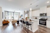 This single-story residence is designed around an open-concept floor plan that seamlessly connects the kitchen, dining, and living areas into one cohesive, light-filled space. Rich wood-look flooring flows throughout the main living areas, grounding the bright, neutral palette of soft grays and crisp whites.

The kitchen is a central highlight, showcasing white shaker cabinetry extending to the ceiling, granite countertops, and a classic subway tile backsplash. A generous island with seating for multiple guests serves as both a prep space and a social hub, illuminated by sleek pendant lighting. Stainless steel appliances, including a gas range, over-the-range microwave, and full-size refrigerator, complete the well-appointed cooking space.

The living room benefits from an abundance of natural light streaming through large windows and a glass door, creating an airy, welcoming atmosphere enhanced by a ceiling fan overhead.

The bedrooms offer a calm retreat, each carpeted for comfort and sized to accommodate generous furnishings. The primary bedroom connects to a bathroom featuring granite-topped vanity cabinetry and a walk-in closet, while wood-look flooring carries through the bathroom and hallway spaces. The overall ambiance throughout is clean, contemporary, and move-in ready.