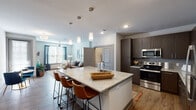 This well-appointed two-bedroom, two-bathroom residence offers a thoughtfully designed single-level layout with modern finishes and a comfortable, contemporary ambiance. The open-concept kitchen serves as the centerpiece of the living area, anchored by a large granite-topped island with an integrated sink and seating for multiple guests. Pendant lighting hangs above the island, complementing the dark espresso cabinetry, stainless steel appliances, and wood-look flooring that extends throughout the main living spaces.

The adjoining living room benefits from multiple windows that invite abundant natural light, with a ceiling fan overhead and direct access to a private exterior door. The primary bedroom is generously sized, featuring plush carpeting, a ceiling fan, large windows, and a private en-suite bathroom. The primary bath is notably well-equipped, offering a dual-sink granite vanity, a soaking tub, and a separate glass-enclosed shower. The second bedroom also features carpeted flooring and a bright window. A second full bathroom with a granite vanity and tub-shower combination serves this bedroom. Throughout, neutral tones and clean architectural lines create a cohesive, modern living environment.