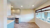 This thoughtfully designed single-floor unit offers a clean, contemporary aesthetic throughout. Light wood-look flooring flows seamlessly across the open-plan living and dining areas, complemented by neutral cream-toned walls and recessed lighting that creates a bright, welcoming atmosphere. Multiple windows fitted with dark Roman shades invite natural light while maintaining privacy, with views of the surrounding neighborhood.

The galley-style kitchen is a standout feature, showcasing high-gloss taupe cabinetry that extends to the ceiling for ample storage, paired with crisp white quartz countertops and a subway tile backsplash. Stainless steel appliances — including a refrigerator, range, microwave, and dishwasher — lend a polished, modern finish. An in-unit washer is also conveniently integrated into the kitchen layout.

The living and dining areas offer generous open space, ideal for flexible furniture arrangements. A dedicated bedroom provides a quiet retreat, equipped with a wall-mounted air conditioning unit and a window overlooking neighboring rooftops.

The bathroom is finished to a high standard, featuring large-format white floor tiles, sleek wall-hung cabinetry, and a glass-enclosed walk-in shower clad in elegant large-format stone-look tile. The entry foyer is bright and welcoming, framed by dual windows and a modern front door with keypad access.