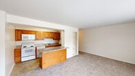 Located at 5597 Heritage Court Dr in Wilmington, Delaware, this two-bedroom, one-bathroom residence offers a practical and well-organized single-floor layout. The combined kitchen and living area forms the heart of the home, with the kitchen featuring warm honey-toned wood cabinetry, granite-style laminate countertops, a peninsula breakfast bar, tile flooring, and white appliances including a range, built-in microwave, and dishwasher. A built-in shelving unit adds functional storage at the transition into the living room, which is carpeted and filled with natural light through a wide triple-pane window overlooking the surrounding community. Both bedrooms are carpeted and finished in neutral tones, providing a calm and comfortable atmosphere. The primary bedroom offers generous floor space and a full-width double-door closet, while the second bedroom includes a window that brings in natural light and a standard closet. A hallway connects the private areas of the home, leading to the full bathroom, which is equipped with a clean white tub-shower combination. Throughout the residence, the consistent use of neutral wall colors, carpet, and clean white trim creates a cohesive and move-in-ready environment.