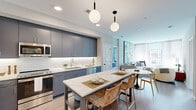 Located at 7200 Baltimore Ave in College Park, Maryland, this single-floor residence offers a thoughtfully designed open-concept layout with modern finishes throughout. The kitchen is a standout feature, showcasing slate-blue cabinetry with under-cabinet lighting, a white subway tile backsplash, stainless steel appliances, quartz countertops, and a central island with seating — all illuminated by stylish globe pendant lighting. Light wood-tone flooring flows seamlessly into the adjoining living and dining areas. The living room is bright and welcoming, with large windows allowing generous natural light and views of the surrounding neighborhood. It offers ample room for comfortable seating arrangements. The bedrooms are calm and restful, with neutral tones, large windows, and light wood flooring. The primary bathroom features a double vanity with quartz counters, grey tile flooring, and a glass-enclosed shower, while the secondary bathroom includes a full tub-shower combo with classic white subway tile surround and grey tile floors. Throughout the residence, clean lines, contemporary fixtures, and a cohesive cool-neutral palette create a polished, modern ambiance well-suited for everyday living in College Park.
