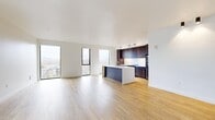 Located on West Main Street in Charlottesville, Virginia, this contemporary one-bedroom, two-bathroom residence offers a thoughtfully designed single-floor layout with a clean, modern aesthetic throughout. Light hardwood flooring flows continuously across the space, complementing crisp white walls and creating a warm yet minimal atmosphere.

The open-concept living and kitchen area serves as the heart of the unit. The kitchen features rich dark wood cabinetry extending floor-to-ceiling, white quartz countertops, stainless steel appliances, and a striking two-tone island with an integrated sink—ideal for both cooking and casual dining. Tall, narrow floor-to-ceiling windows flood the space with natural light while framing elevated views of the Charlottesville cityscape and the Blue Ridge Mountains beyond.

The generously sized primary bedroom includes sliding doors, ample closet space with built-in shelving, and a vertical window offering additional city views. Two well-appointed bathrooms feature contemporary vanities with dark cabinetry and modern fixtures. The layout also includes two hallways, a utility room, and dedicated closet space, ensuring functional storage throughout. The overall ambiance is polished, airy, and well-suited for modern urban living.