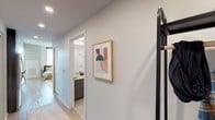 Located at 200 E Fillmore St in the heart of Phoenix, AZ, this modern single-floor studio offers a thoughtfully designed open layout that maximizes functionality and style. The main living and sleeping area features warm wood-tone flooring, a bold dark accent wall, and a ceiling fan that enhances the contemporary aesthetic. A tall window allows natural light to fill the space, creating a bright and welcoming atmosphere. The room comfortably accommodates both a sleeping area and a sitting area, making efficient use of the open floor plan.

The kitchen is outfitted with dark wood cabinetry, stainless steel appliances including a gas range and microwave, and a clean white countertop that extends seamlessly into a built-in desk workspace — an ideal setup for those who work from home. Upper shelving provides additional storage and display space above the workstation.

The bathroom is finished with light tile flooring and clean white walls, offering a calm and functional space. A hallway connects the main living area to the bathroom and entry, lined with recessed lighting and accented with contemporary wall art. Near the entry, a coat rack and open shelving provide practical storage solutions. The overall design balances modern finishes with warm, livable details throughout.