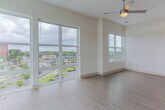 Located at 1850 Merchant Ln in Hampton, Virginia, this single-floor residence offers a well-designed, contemporary layout finished with light wood-style flooring throughout. The open-concept living area is generously sized, bathed in natural light through large floor-to-ceiling sliding glass doors and additional windows that offer outdoor views of the surrounding Hampton cityscape. A ceiling fan keeps the space comfortable year-round.

The kitchen is a standout feature, showcasing rich dark cabinetry, granite-style countertops, a classic subway tile backsplash, stainless steel appliances including a refrigerator, microwave, and range, and stylish pendant lighting overhead. A wide breakfast bar peninsula connects the kitchen seamlessly to the living space.

The bedrooms are bright and airy, each equipped with ceiling fans and windows that invite natural light. One bedroom includes a closet with sliding panel doors. The bathrooms are clean and modern, featuring granite-topped vanities with dark wood cabinetry, tiled soaking tubs, and accessible grab bars. In-unit laundry with a stacked washer and dryer adds everyday convenience. The overall aesthetic is crisp and contemporary, with a neutral white and warm wood palette throughout.