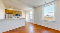 Located at 901 S 5th St in Lynchburg, Virginia, this 2-bedroom, 2-bathroom unit offers a thoughtfully designed single-floor layout. The open-concept kitchen and living area serves as the heart of the space, featuring warm hardwood floors that run throughout, crisp white walls, and an abundance of natural light from multiple large windows with views of the surrounding neighborhood. The kitchen is equipped with stainless steel appliances, light wood cabinetry, white quartz countertops, and a peninsula island with a gold-toned faucet and pendant lighting overhead, creating a functional and stylish cooking area. Both bedrooms continue the hardwood flooring and bright, airy aesthetic, each benefiting from generous windows and recessed lighting. The primary bedroom includes a double closet with gold hardware. The two bathrooms are finished with striking dark penny tile floors, light wood vanities, white quartz countertops, and brushed gold fixtures throughout. One bathroom features a full tub-shower combination with a wall-mounted gold showerhead, while the second offers a vanity with a round mirror and wall sconce. Additional spaces include a laundry room, utility room, and two closets, ensuring practical storage throughout.