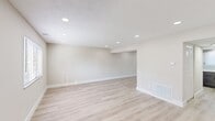 This two-floor home offers a functional and modern layout across five bedrooms and two full bathrooms. The main floor features a bright, open living area finished with light hardwood-style flooring and recessed lighting set into a textured ceiling, creating a clean and airy atmosphere. The kitchen is equipped with dark gray shaker-style cabinetry, white quartz countertops, a stainless steel sink with a matte black faucet, subway tile backsplash, and a stainless steel refrigerator, complemented by a window that brings in natural light. Both bathrooms are finished with a cohesive modern aesthetic, showcasing dark wood vanities, white integrated sinks, matte black fixtures, and rounded rectangular mirrors with sleek black frames. The bedrooms are spread across both floors and feature neutral wall tones throughout. Some bedrooms offer light hardwood-style flooring with recessed lighting, while others are carpeted and include built-in closets with standard rod and shelf configurations. Hallways connect the rooms efficiently, with staircases linking the two floors. The overall design is clean, contemporary, and move-in ready, with consistent use of neutral palettes and matte black hardware accents tying the aesthetic together throughout.