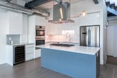 Located at 316 W 200 S in the heart of downtown Salt Lake City, this contemporary two-story loft blends industrial aesthetics with modern finishes across two well-proportioned floors. Exposed ductwork, concrete-textured walls, and open ceilings with ceiling fans give the space a distinctive urban character throughout.

The main level opens into a generous living area bathed in natural light, with wide-plank light hardwood flooring and large sliding glass doors that lead to an outdoor space with direct views of the Salt Lake City skyline. The gourmet kitchen is a standout feature, showcasing high-gloss white cabinetry, a striking blue island with quartz countertops, stainless steel appliances including a double wall oven and French door refrigerator, a subway tile backsplash, and a wine cooler.

A dramatic open-tread staircase with a glass railing connects the two floors, serving as both a functional and architectural centerpiece. The upper level features a spacious carpeted room with double closet doors and exposed industrial piping, adding to the loft's authentic character. Two well-appointed bathrooms serve the space — one featuring a floating dual vanity, a glass-enclosed soaking tub, and large-format tile, while the second offers a walk-in shower and floating vanity with clean, minimalist finishes.