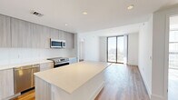 Located in Miami's vibrant Coconut Grove neighborhood, this modern 3-bedroom, 2-bathroom residence offers a thoughtfully designed open-concept layout with contemporary finishes throughout. Light wood-tone flooring flows seamlessly across the living spaces, complementing the clean white walls and recessed lighting that create a bright, airy atmosphere.

The kitchen is a standout feature, boasting a large central island with quartz countertops, sleek light wood cabinetry, and a full suite of stainless steel appliances including a French door refrigerator, range, microwave, and dishwasher. The kitchen opens directly into the living area, making it ideal for entertaining.

Floor-to-ceiling sliding glass doors in the living room and select bedrooms flood the space with natural light and offer sweeping views of the Miami skyline and surrounding cityscape. The bedrooms are well-proportioned, each featuring wood flooring and generous natural light, with the primary bedroom benefiting from direct balcony access and a dedicated closet.

Both bathrooms are finished in a contemporary style, featuring glass-enclosed walk-in showers with mosaic tile flooring, light tile surrounds, and modern vanities. The primary bath connects to a spacious walk-in closet. Clean lines and a neutral palette define the overall design, creating a polished, move-in-ready residence.