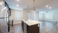 Located at 1711 E Centerton Blvd in Centerton, Arkansas, this well-appointed single-floor residence offers a thoughtfully designed open-concept layout with modern finishes throughout. The kitchen serves as a central highlight, featuring rich dark cabinetry, a light-toned quartz countertop island with an integrated double sink, stainless steel appliances including a refrigerator, range, and microwave, and a stylish glass tile backsplash. Sleek pendant lights hang above the island, adding a contemporary touch. The living and dining areas flow seamlessly from the kitchen, showcasing durable wood-look flooring, ceiling fans, and generous natural light through multiple windows with blinds. The bedrooms are finished with plush wall-to-wall carpeting and ceiling fans, providing a comfortable and quiet retreat. One bedroom opens directly to a private balcony through sliding glass doors, offering outdoor access and views of the surrounding community. The bathroom is clean and functional, appointed with large-format tile in the tub/shower surround, tile flooring, and dark cabinetry for storage. Throughout the space, neutral tones and recessed lighting create a bright, cohesive ambiance suited for modern living.